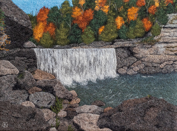 Felted wool artwork of a waterfall, as seen from a rocky shore and with red, orange, yellow, and green trees in the background