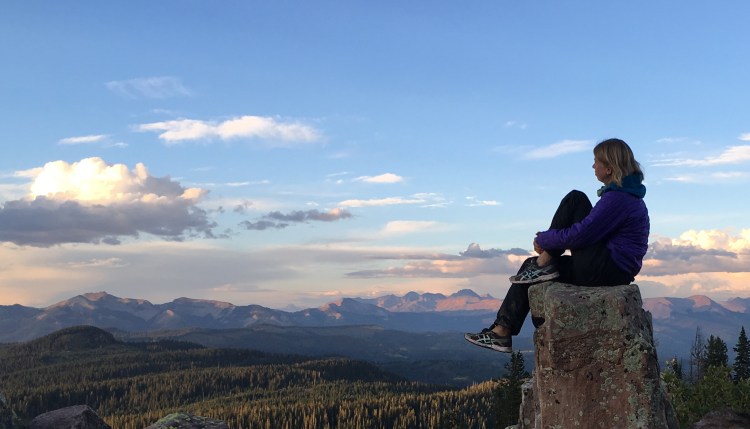 A hiker sitting on a rock and looking out across mountain ridges at sunset