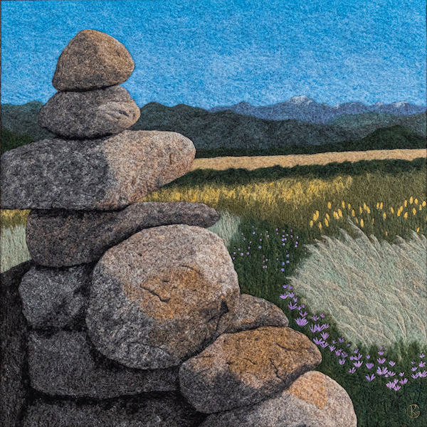 Felted wool artwork of a stack of rocks with mountains in the background
