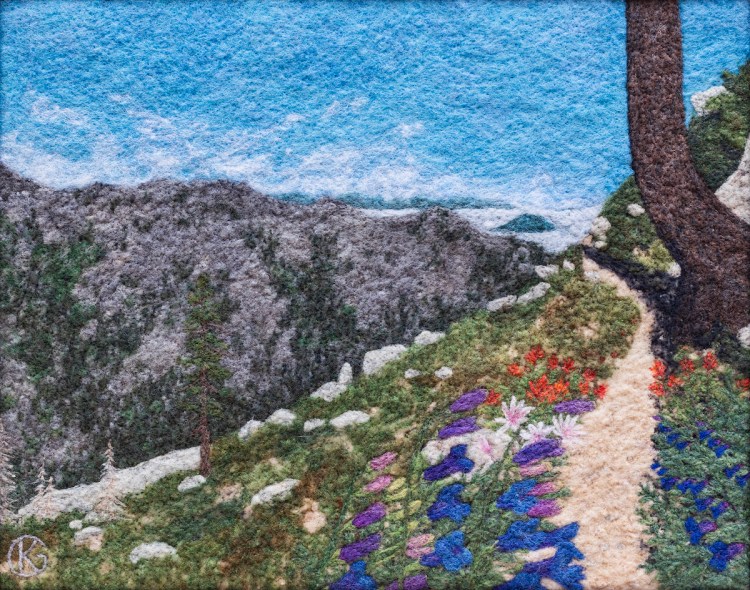 Felted wool artwork of a sloped mountain trail, with blue, white, and red flowers growing trailside.